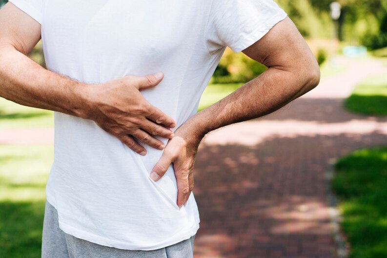 A man in a park appears to be experiencing back pain, possibly seeking help from an orthopedic doctor in Talwandi Kota.jpeg