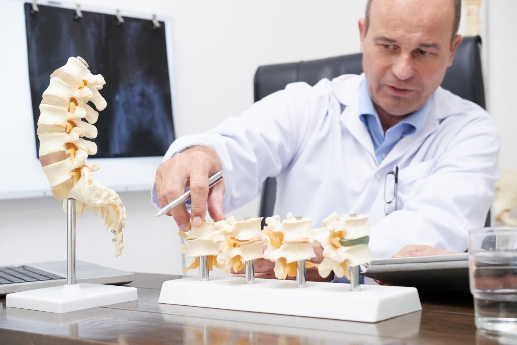 A man in a lab coat examines a detailed model of a spine, showcasing his expertise in orthopedic medicine.jpeg